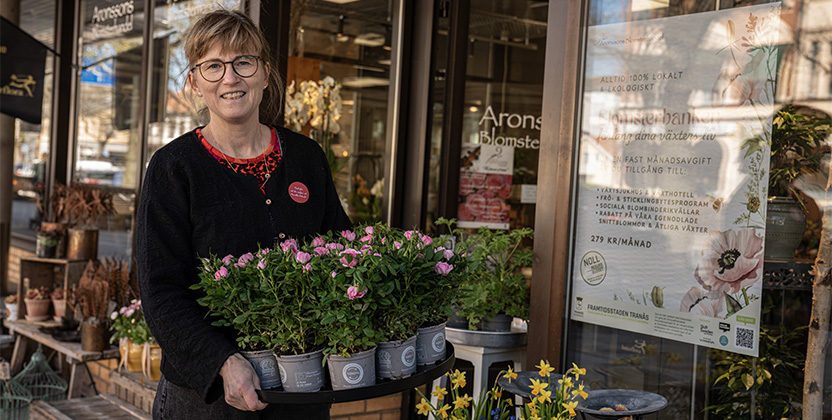 En kvinna framför en butik, hållande en kruka med blommor.