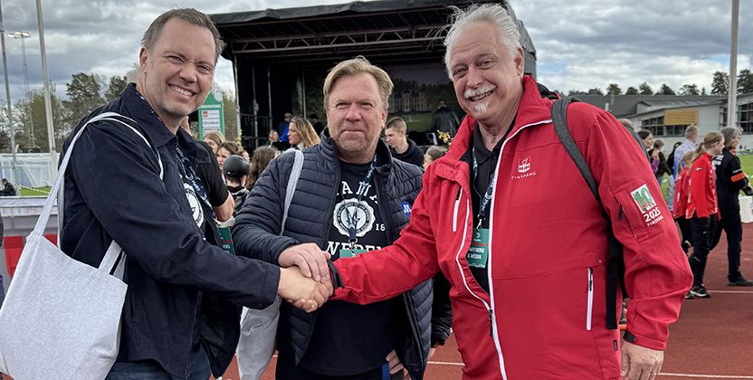 Tre män på en idrottsarena tar i hand.