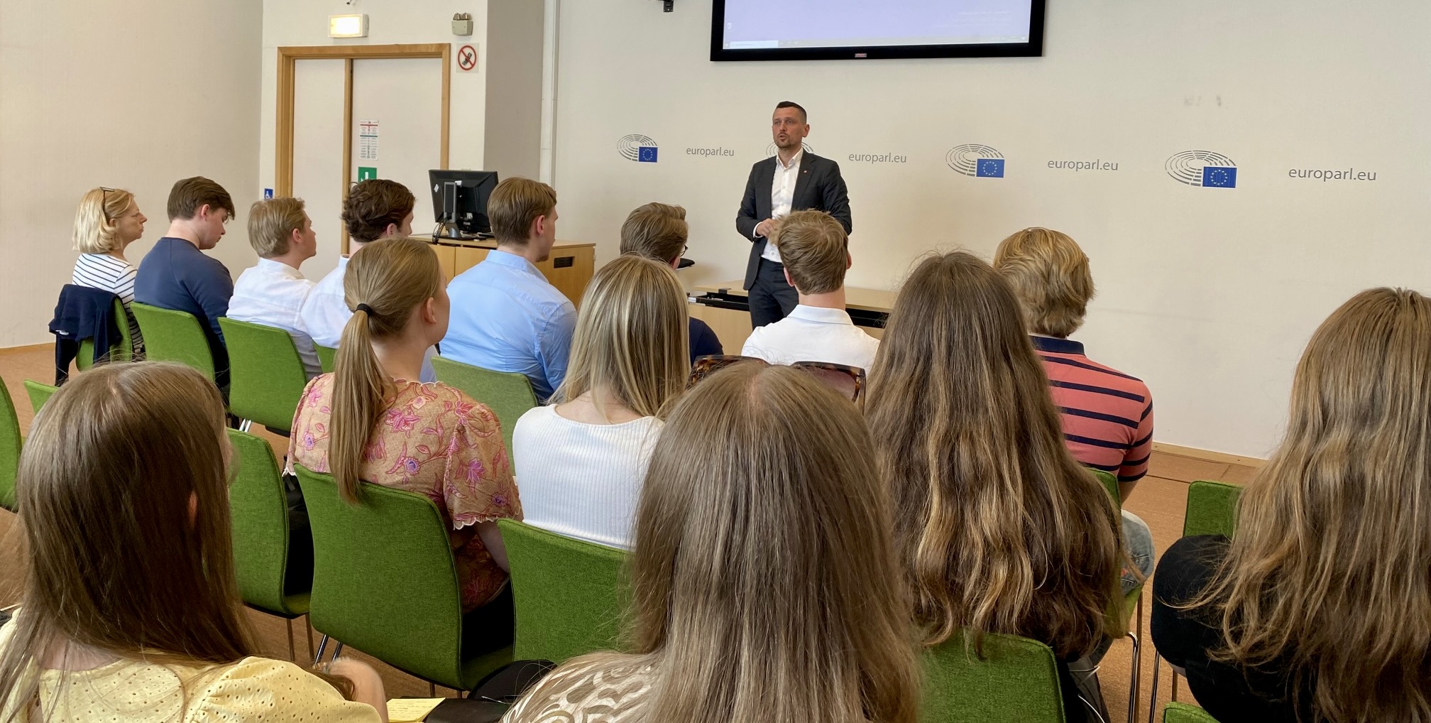 En man håller föredrag inför en grupp människor som sitter på stolar framför honom.