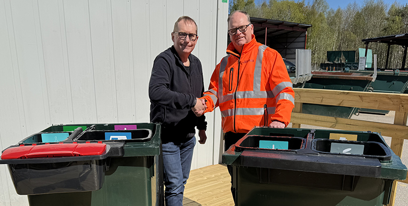 Två män står vid två avfallskärl på en återvinningscentral.