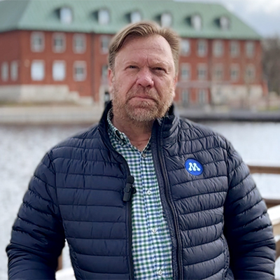 En man framför ett vattendrag och en pampig byggnad. 