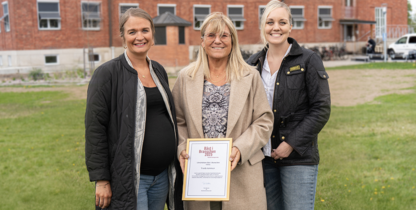 Tre leende kvnnor framför stadshuset, de håller i ett diplom.