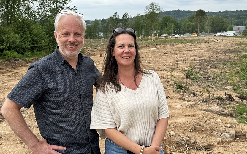 Två personer framför ett naturområde där det grävs i marken. I bakgrunden skymtar maskiner och byggnader 