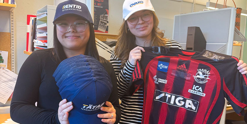 Två personer i keps. Den ena håller i kepsar och den andra håller i en fotbollströja.