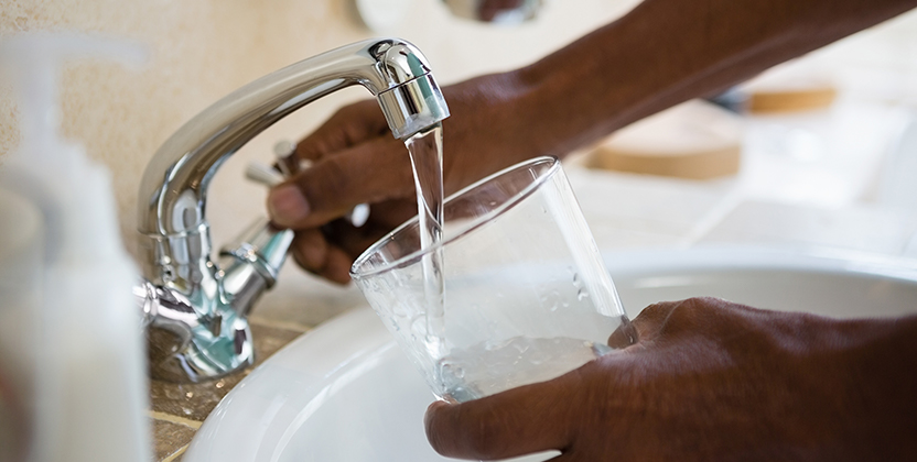 En person som häller upp kranvatten i ett dricksglas.