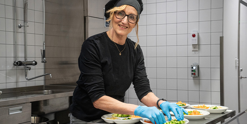 Person som lägger upp sallad på tallrikar i ett skolkök.