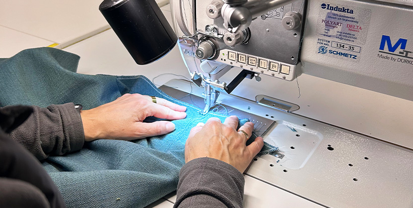Två händer som syr med ett blått tyg i en symaskin.