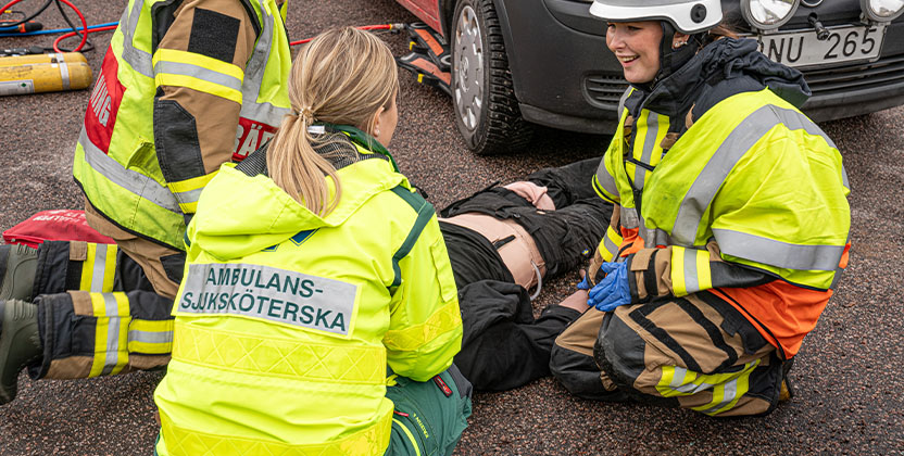 Räddningspersonal och ambulanssjuksköterska hjälper en person på marken vid en bilolycka.