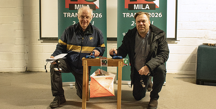 Två män står på huk vid en orienteringskontroll.