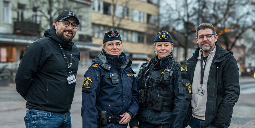 Två personer tillsammans med två poliser som kollar in i kameran och ler.