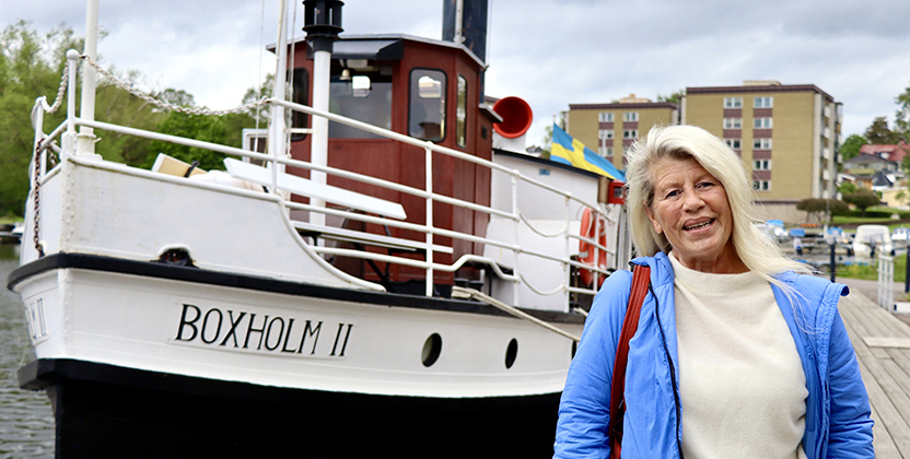 En ångbåt ligger förtöjd vid en brygga. Framför den står en kvinna.