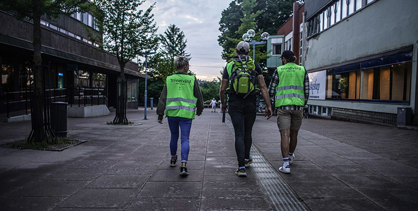 Tre personer i gröna västar på en mörk gata