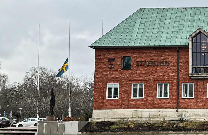 Svensk flagga hissad på halv stång vid en tegelbyggnad.